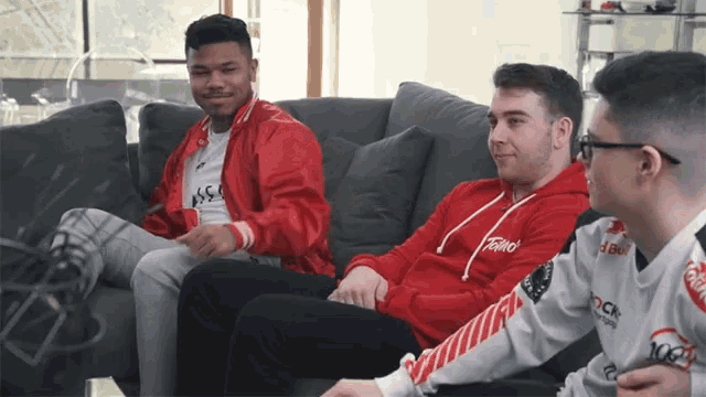 three men are sitting on a couch and one of them is wearing a red hoodie that says toro