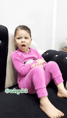a little girl in a pink outfit sits on a black couch with the hashtag @ wkp38