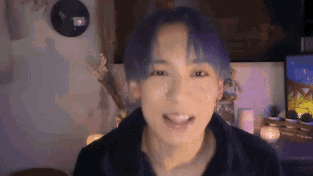 a young man with blue hair is smiling for the camera in a room .