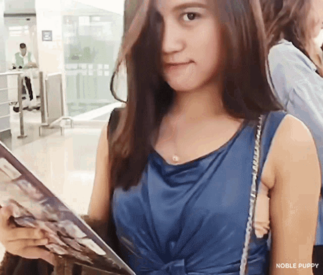 a woman in a blue tank top is holding a magazine with noble puppy written on the bottom right