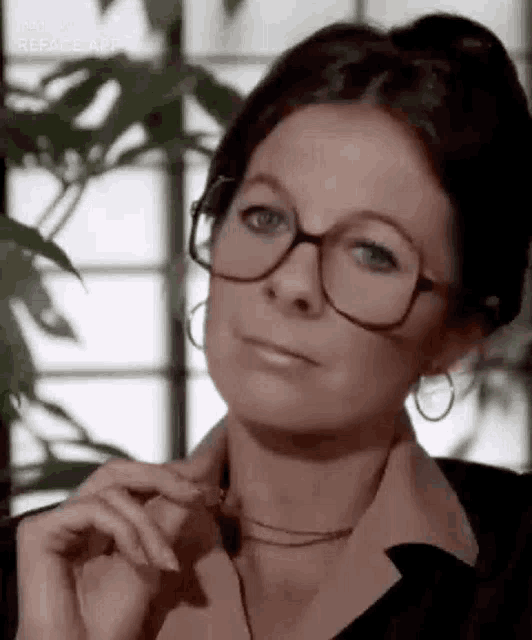 a woman wearing glasses and hoop earrings is looking at the camera with her hand on her chin .