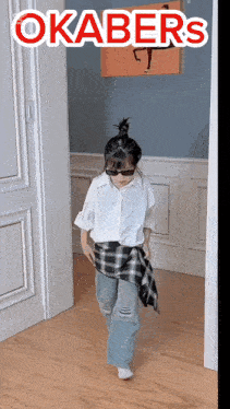 a little girl wearing sunglasses and a plaid shirt is standing in a hallway with the word okabers on the bottom right