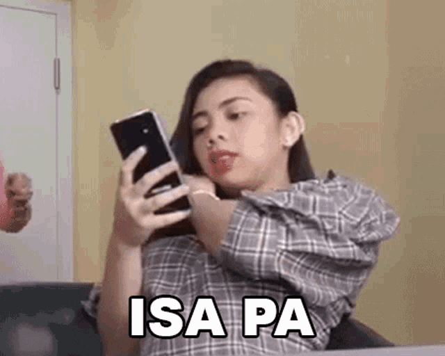 a woman in a plaid shirt is sitting on a couch looking at her cell phone .