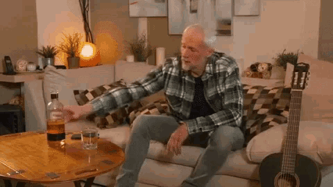 a man is sitting on a couch with a bottle of whiskey and a glass of whiskey on a table .