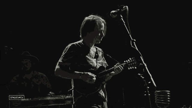 a man playing a guitar in front of a microphone with stagecoach written on the bottom right