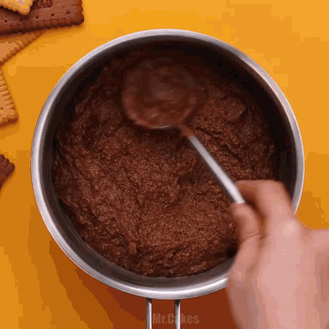 a person is mixing a chocolate sauce with a spoon in a pot that says mr.cakes