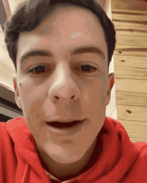 a man wearing a red hoodie looks at the camera with his mouth open