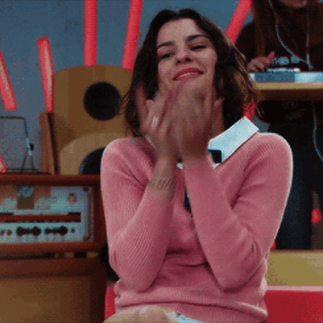 a woman wearing a pink sweater is smiling and clapping her hands