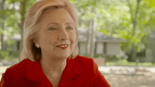 a woman wearing a red shirt and earrings smiles