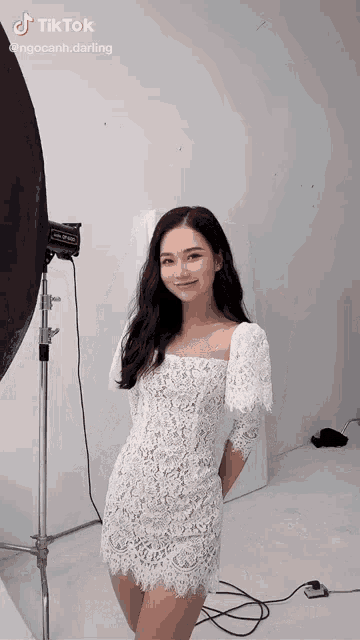 a woman in a white lace dress stands in front of a light
