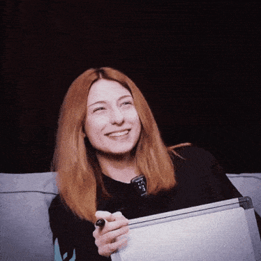 a woman is smiling while holding a white board and a remote control