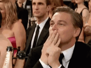 a man in a suit and tie is sitting in a crowd and covering his mouth with his hand .