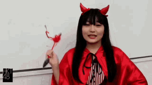 a girl in a red devil costume is holding a knife and feathers .