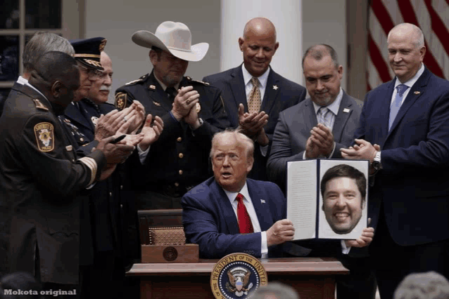 a group of men applaud while a man holds up a picture of a man 's face