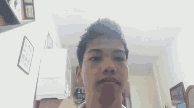 a young man in a white shirt is holding his hair in his hands and looking at the camera .