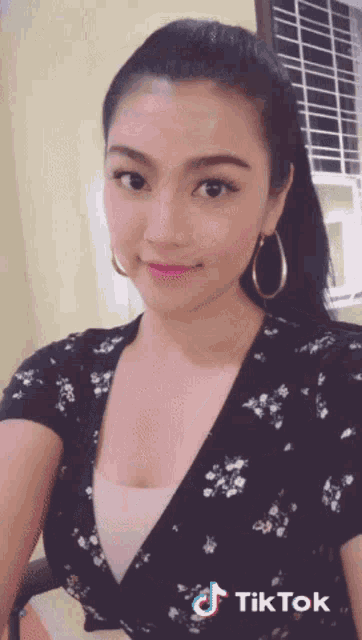 a woman wearing hoop earrings and a floral top has a tiktok watermark on her face