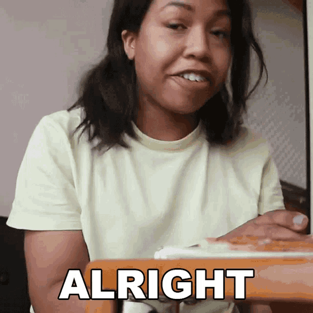 a woman is sitting at a table with a plate of food and the word alright is on the table in front of her