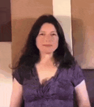 a woman with long dark hair is wearing a purple shirt and sitting on a couch .