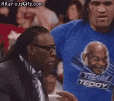 a man wearing a blue shirt that says team teddy is talking to another man