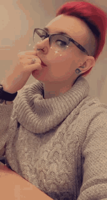 a woman with red hair and glasses is sitting at a table with her hand to her mouth .