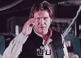 a man in a black vest and white shirt is making a funny face with his hand .