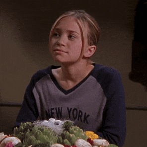 a girl wearing a new york shirt sits at a table with artichokes
