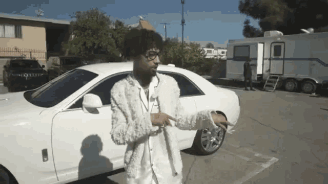 a man in a white jacket is standing in front of a white car