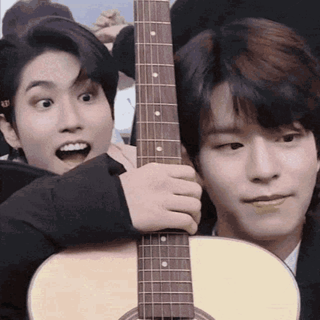 two young men are holding an acoustic guitar and one of them is making a funny face .