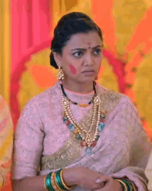 a woman wearing a necklace and earrings is sitting in front of a yellow wall .