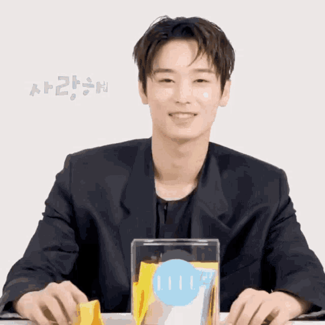 a man in a black jacket is smiling while holding a container with a blue circle on it