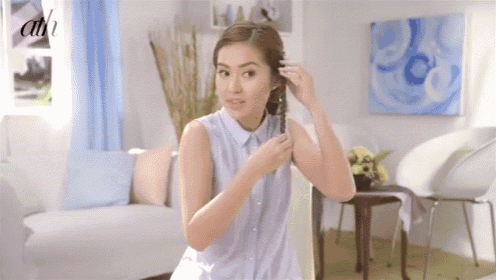 a woman in a purple shirt is brushing her hair in a living room with ath written on the wall