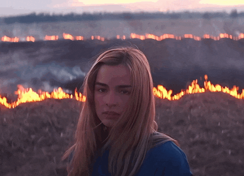 a woman in a blue shirt stands in front of a field of fire