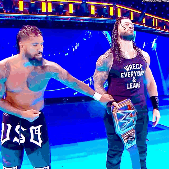two wrestlers standing on a stage with one wearing a tank top that says wreck everyone and leave