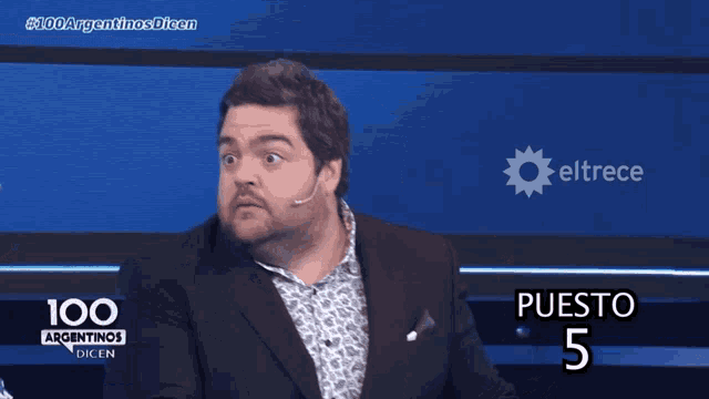 a man in a suit is sitting in front of a screen that says puesto 5