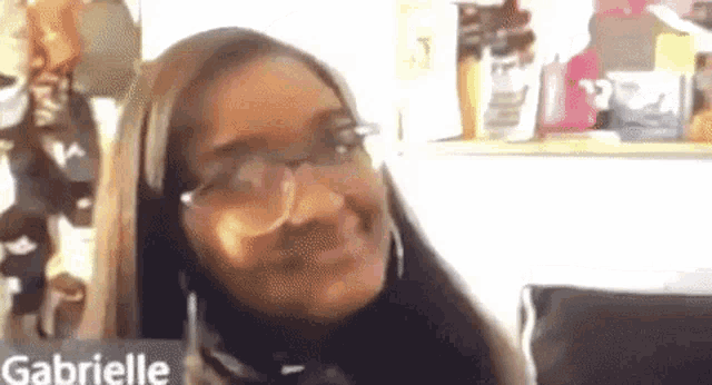 a woman wearing glasses is smiling while sitting on a couch in front of a computer screen .