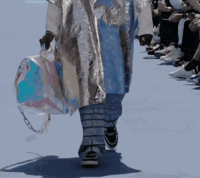 a model is walking down the runway at a fashion show holding a clear bag .