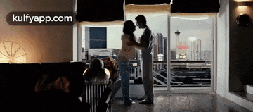 a man and a woman are dancing in a living room in front of a large window .