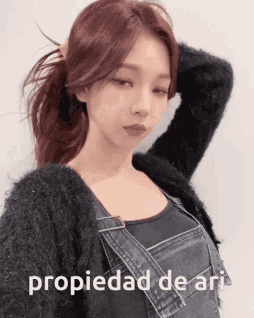 a woman wearing overalls and a black sweater with the word propiedad de ari on the bottom right