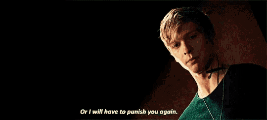 a man in a green shirt is standing in a dark room and saying `` or i will have to punish you again . ''