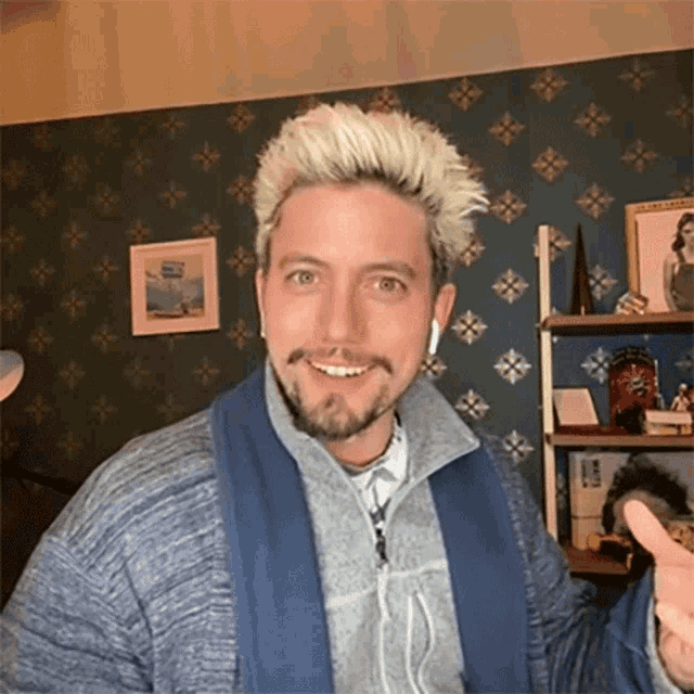 a man with blonde hair and a beard is wearing headphones and a blue sweater .