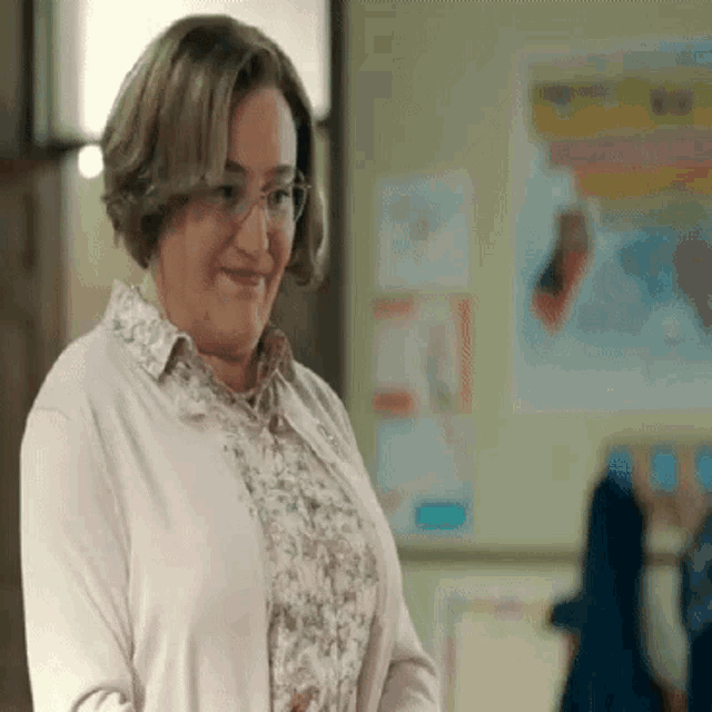 a woman wearing glasses and a pink sweater is smiling .