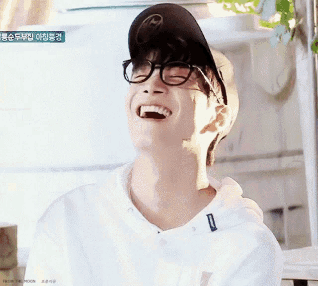 a young man wearing glasses and a baseball cap is laughing with his mouth open .