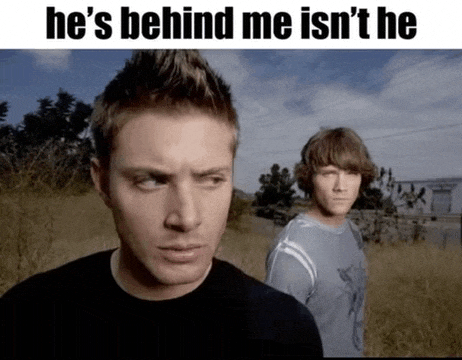 two men are standing next to each other in a field with a caption that says he 's behind me isn 't he
