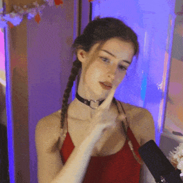 a woman wearing a choker and a red tank top holds her finger to her chin