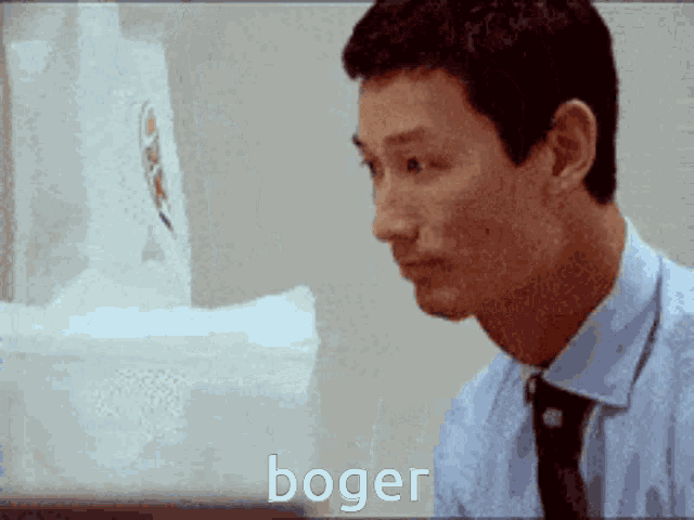 a man in a blue shirt and tie is sitting in front of a box that says boger on it