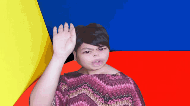 a woman in a purple shirt is waving her hand in front of a colorful background