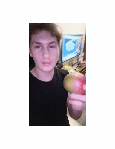 a young man is holding an apple in front of a computer screen .