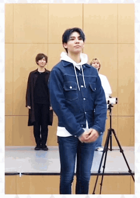 a man in a denim jacket is standing in front of a tripod