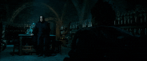 a man in a black coat stands in a dark room with bottles on shelves and a man in a black jacket