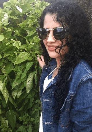 a woman wearing sunglasses and a denim jacket is standing in front of a bush